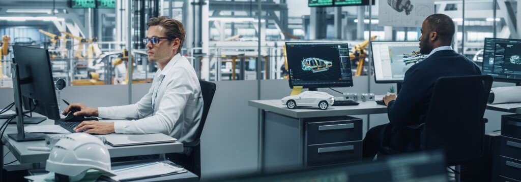 Engineers working at computer workstations with automotive design software, overlooking a factory floor with assembly equipment.