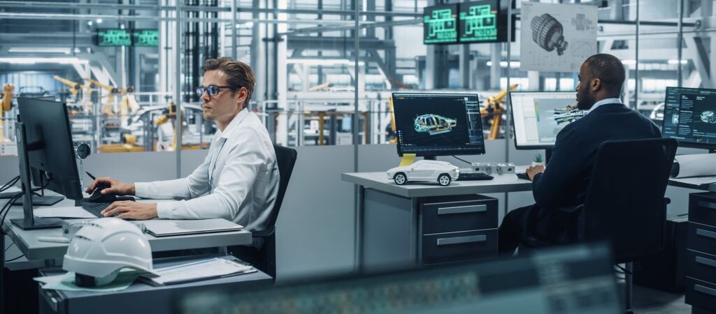 Engineers working at computer workstations with automotive design software, overlooking a factory floor with assembly equipment.