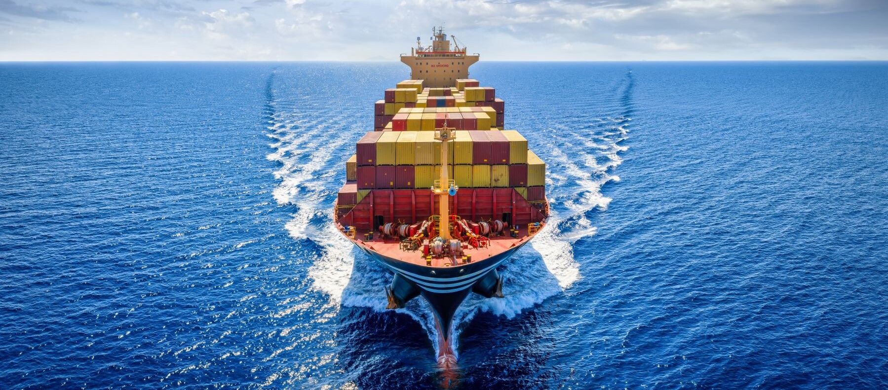 Container ship transporting cargo across the open ocean under a partly cloudy sky