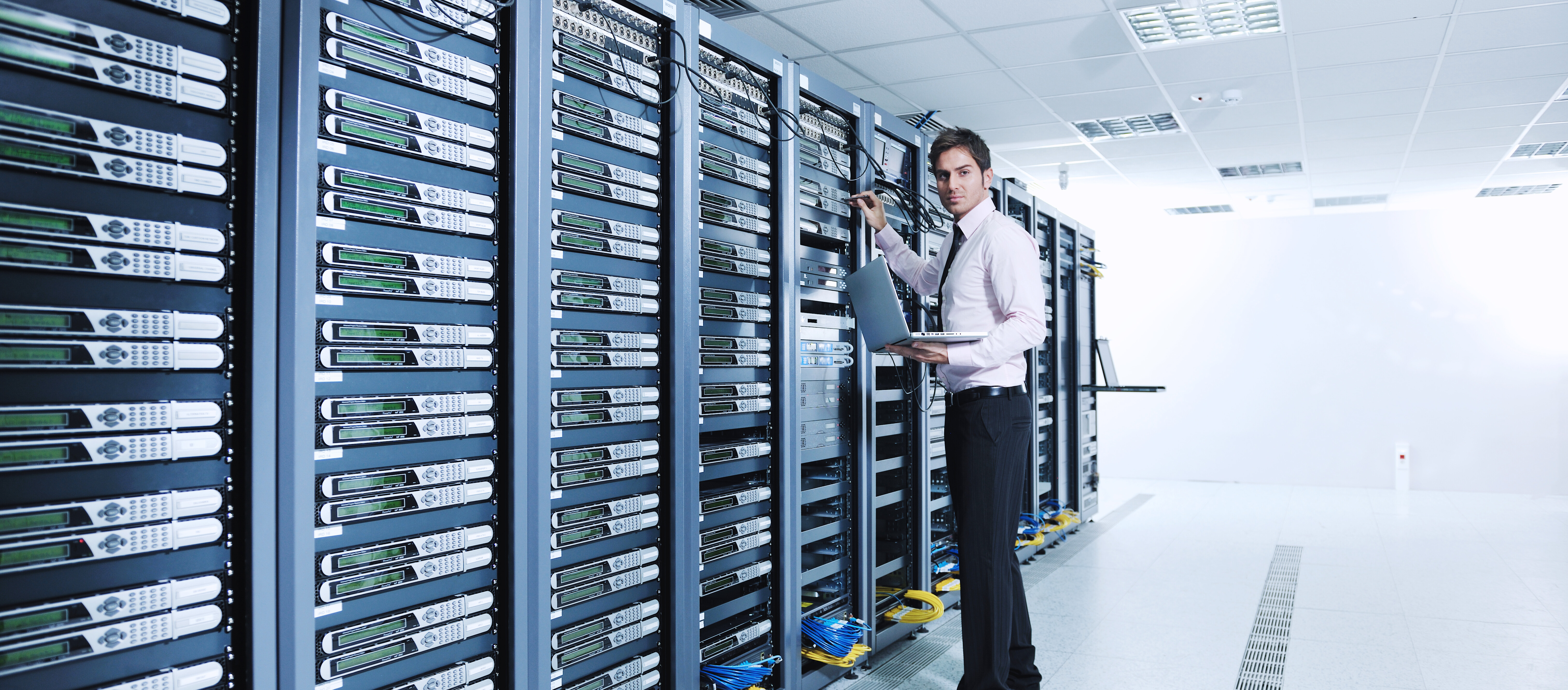 Technician working in a data center aisle with server racks and network equipment.