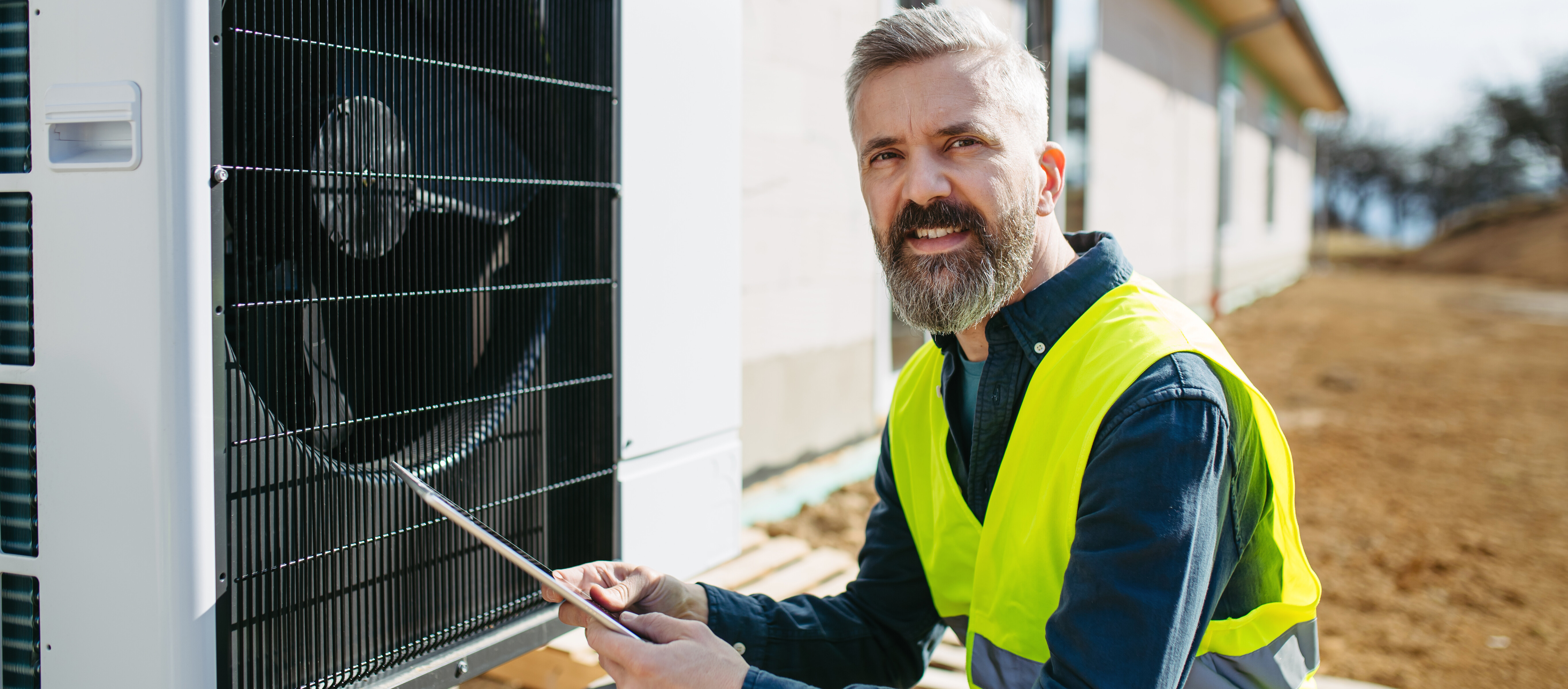 Technicien inspectant une pompe à chaleur extérieure avec une tablette.