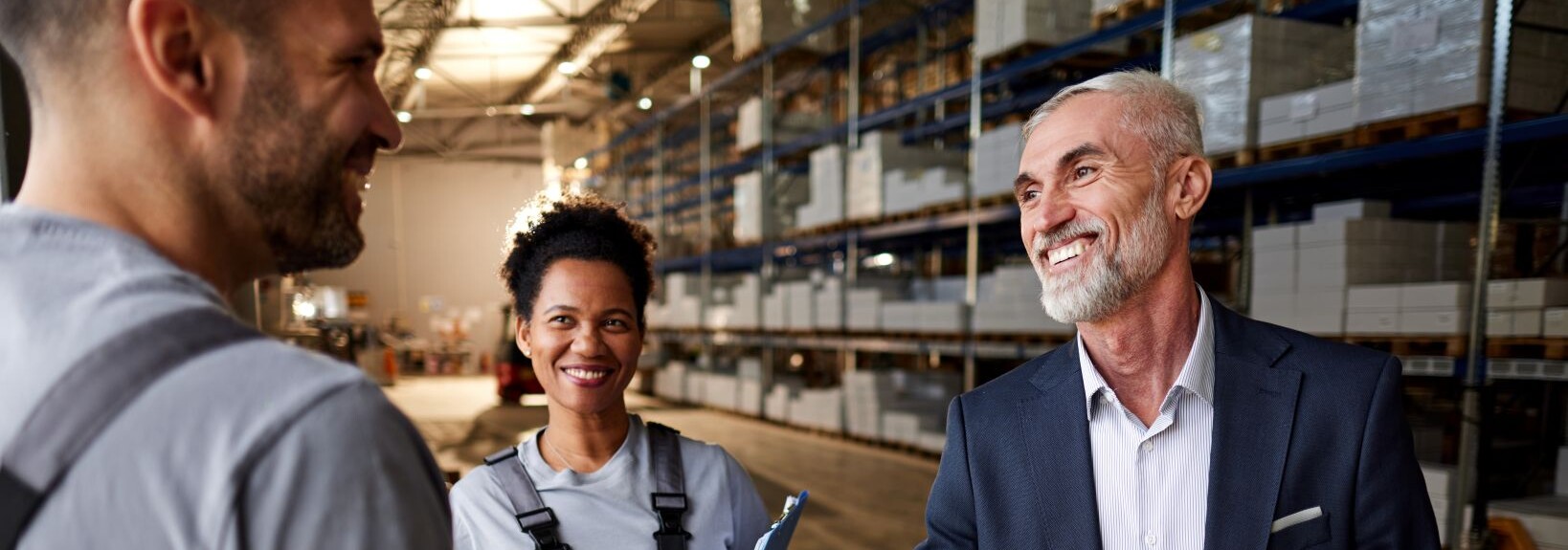Business professional shaking hands with a warehouse worker inside a storage facility.