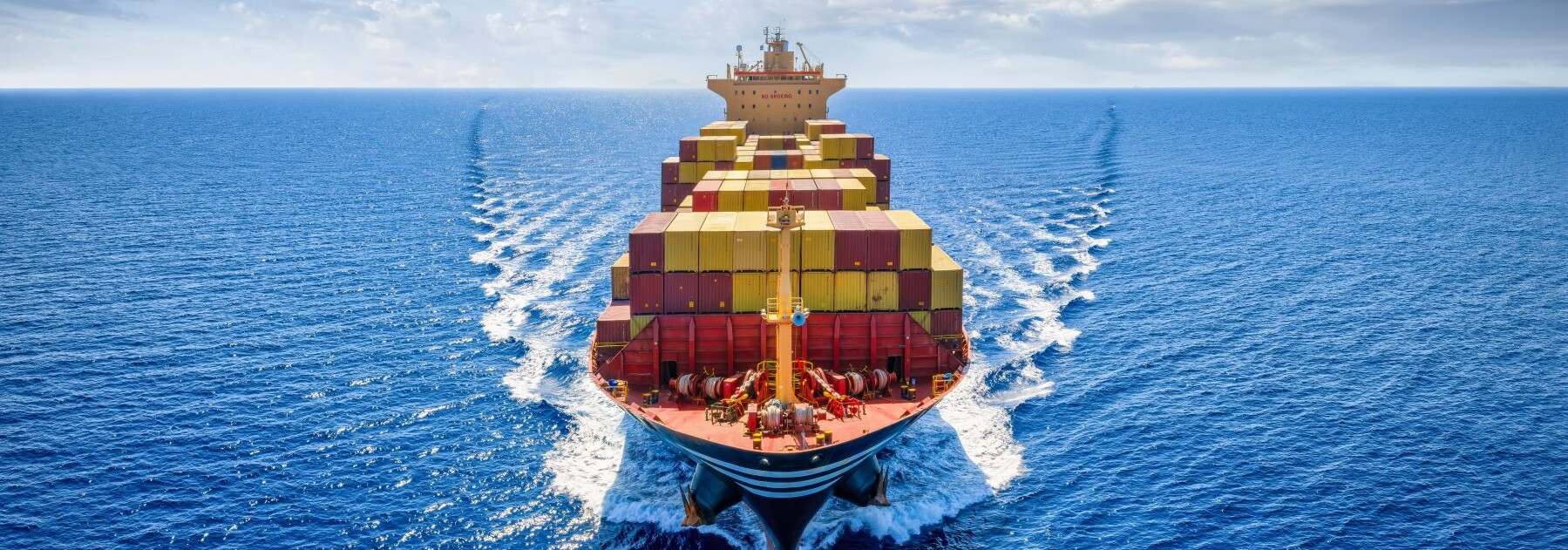 Container ship transporting cargo across the open ocean under a partly cloudy sky