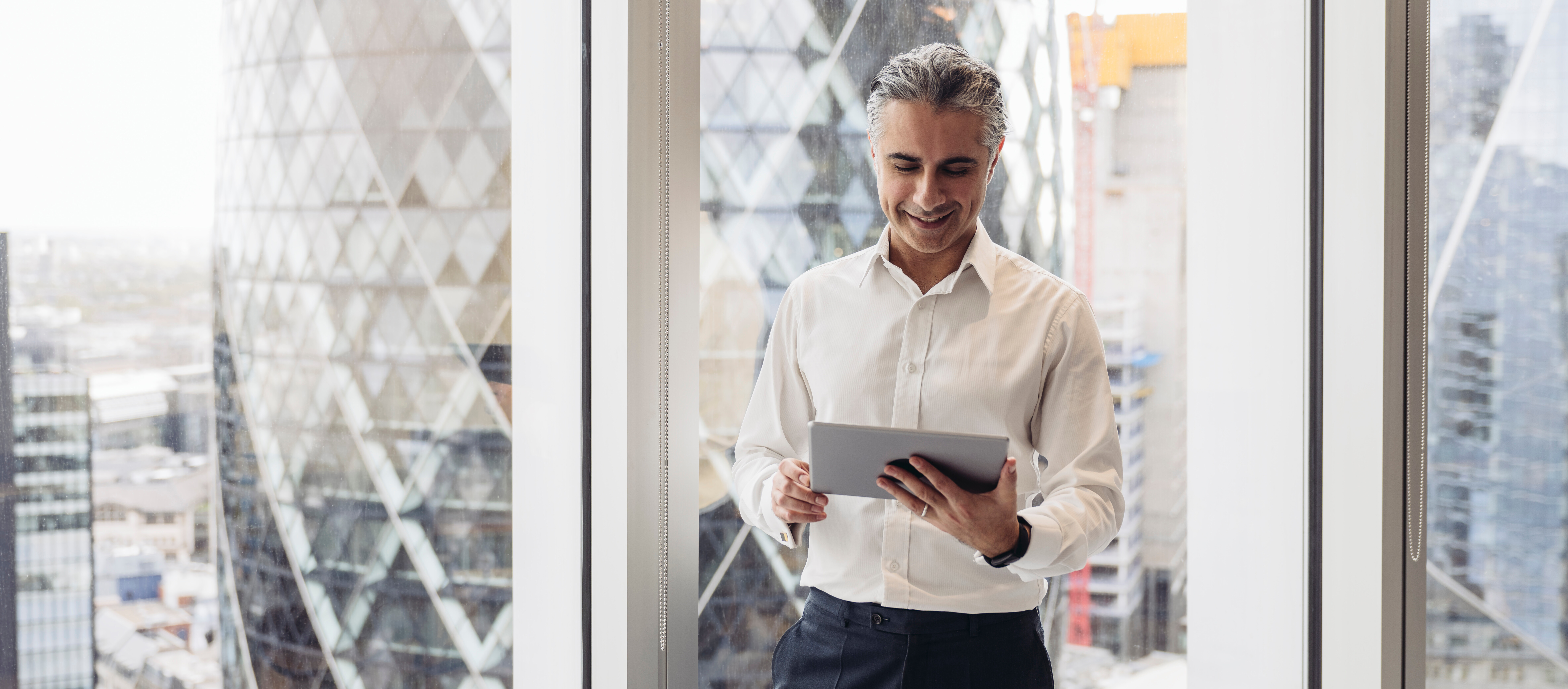Business professional standing by a window, reading information on a tablet.