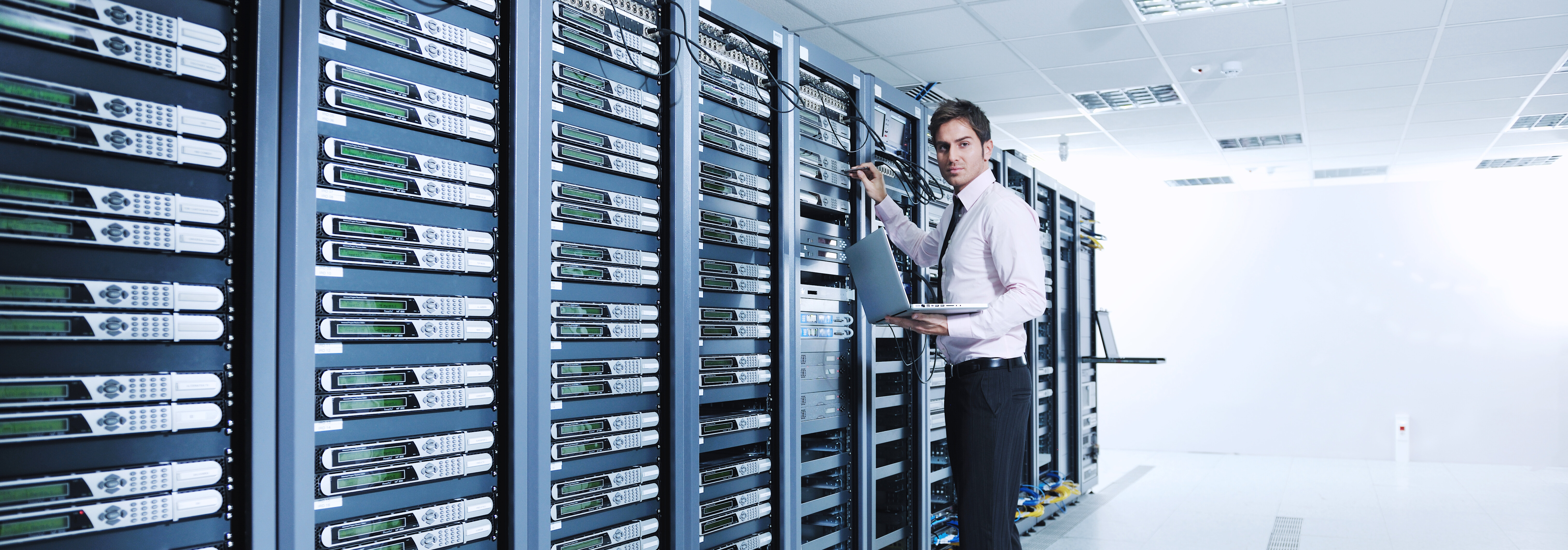 Technician working in a data center aisle with server racks and network equipment.