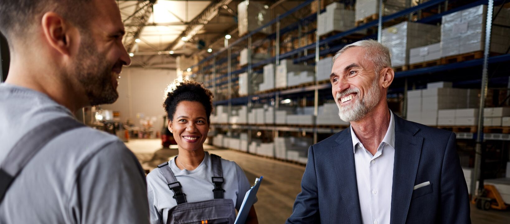 Business professional shaking hands with a warehouse worker inside a storage facility.